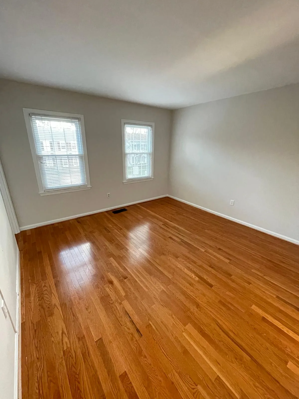 Empty bedroom with clean hardwood floors and two windows